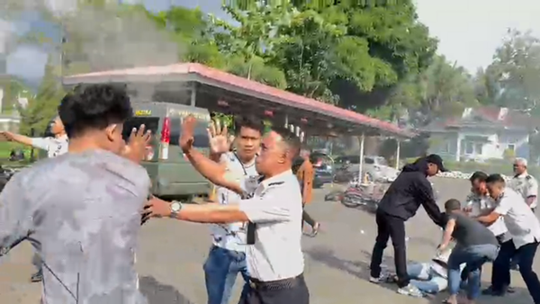 Sejumlah pria berpakaian sipil bersama oknum petugas berseragam putih terlibat aksi saling tarik saat berupaya mengamankan seorang mahasiswa di tanah. Insiden mencekam ini terjadi di tengah aksi unjuk rasa AMPH terkait darurat narkoba yang berakhir rusuh.